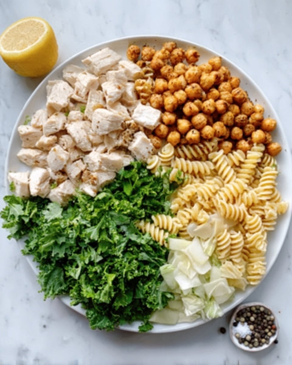 A white plate on a white marbled surface is filled with five different sections of food arranged in a circular pattern. Starting from the left, there's a pile of cooked white chicken pieces with a slightly browned texture. Next to it, roasted chickpeas with a crispy golden-brown color. Above the chickpeas, a section of cooked, pale yellow spiral pasta. Above the pasta, there's a pile of light beige sliced cabbage or a similar vegetable with a soft texture. To the left of the cabbage, fresh green chopped lettuce or kale adds a vibrant color contrast. A lemon wedge and some peppercorns sit on the white marbled surface near the plate. Photo taken with an iphone --ar 4:5 --v 7
