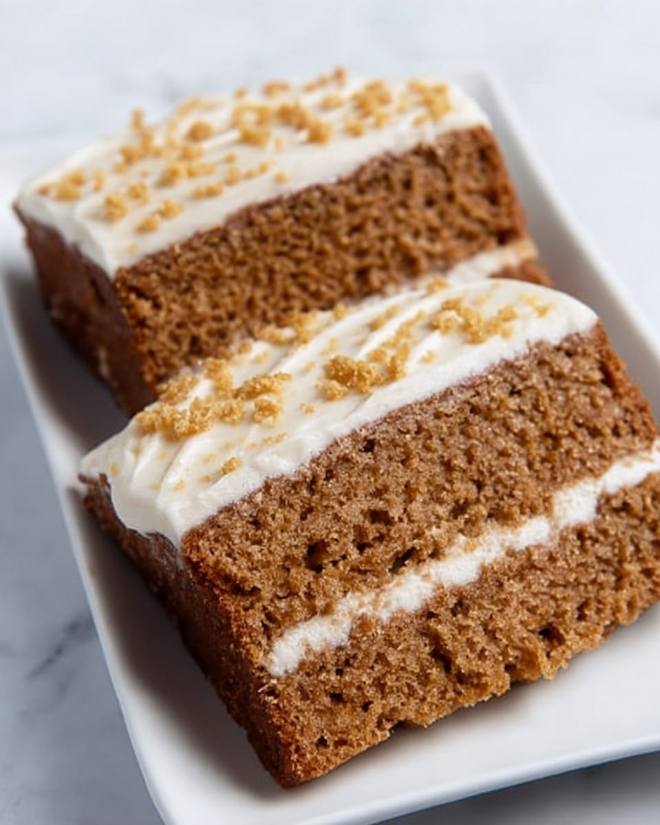 The image shows two slices of brown cake with a moist texture, layered with a thin white cream frosting on top. The frosting has small golden crumbs sprinkled over it. The slices are placed on a white rectangular plate, which is set on a white marbled surface. photo taken with an iphone --ar 4:5 --v 7