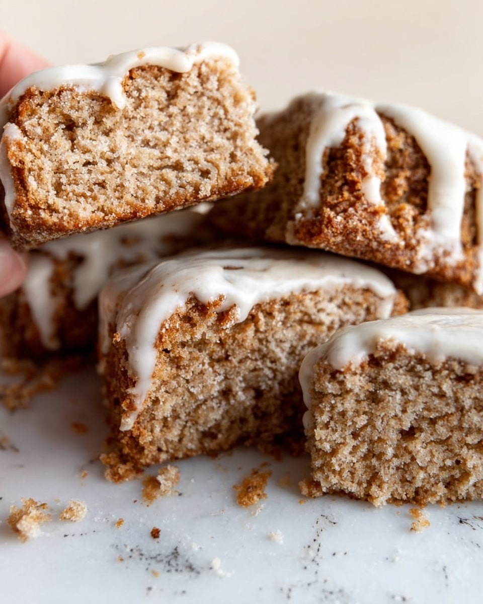 The image shows several pieces of a light brown, crumbly cake with a thick white icing on top. The cake layers are soft and slightly rough in texture, stacked unevenly with some crumbs scattered around. The icing looks smooth and creamy, sitting on top and dripping lightly down the sides of the cake pieces. The cake rests on a white marbled surface. A woman's hand is holding one piece of the cake. Photo taken with an iphone --ar 4:5 --v 7