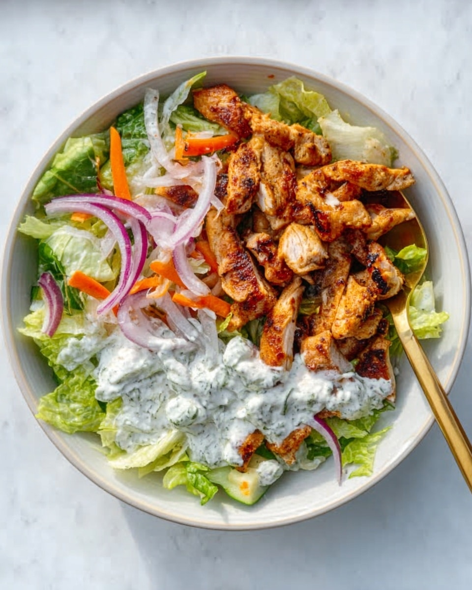 The image shows a white bowl filled with a fresh salad placed on a white marbled surface. The salad has a base layer of green lettuce leaves covering the bottom. On top, there are several pieces of cooked, golden-brown chicken strips arranged mostly on one side. Next to the chicken, there are some orange carrot slices and thin red onion slices mixed with the lettuce. A creamy white dressing with green herbs is spread over one side of the salad, giving a textured look. There is a small gold spoon resting inside the bowl on the edge. Photo taken with an iphone --ar 4:5 --v 7
