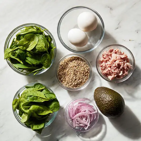 The image shows six clear glass bowls arranged on a white marbled surface. One bowl contains fresh green spinach leaves with a smooth texture, another has two white eggs resting side by side with smooth shells. A third bowl is filled with small beige grains with a rough texture. Another bowl holds a large avocado with a dark, bumpy skin. There is a bowl containing small pink and white pieces that look like chopped meat, and a small bowl with thinly sliced red onion rings. The bowls are neat and the colors contrast well against the white marbled surface. Photo taken with an iphone --ar 4:5 --v 7