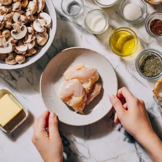 The image shows two raw chicken pieces placed on a white plate at the bottom center. Above the plate, there is a small cube of butter on the table. On the top left, a white bowl filled with sliced mushrooms is visible. Around these items, various small glass containers with cooking ingredients like milk, oil, and spices are arranged on a white marbled surface. A woman's hand is not visible in the image. Photo taken with an iphone --ar 4:5 --v 7