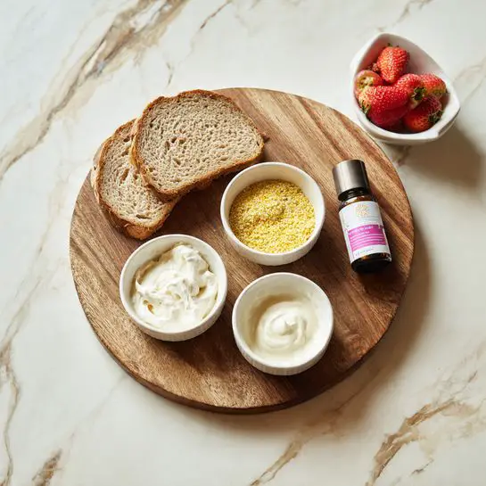 The image shows a round wooden board on a white marbled surface with three thick slices of light brown bread stacked in the top left. On the board, there are three small white bowls: one with a thick white spread, one with yellow granules and white cream, and one with a smooth cream-colored liquid. A small dark bottle with a pink label is placed between the bowls. In the top right corner of the image, a white bowl with fresh red strawberries is partially visible. photo taken with an iphone --ar 4:5 --v 7
