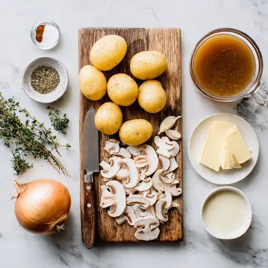 The image shows a wooden cutting board on a white marbled surface with several ingredients arranged neatly. On the board, there are five whole yellow potatoes near the top, a cluster of thinly sliced white mushrooms spread across the lower half, a whole brown onion placed to the left, and three garlic cloves below the potatoes. A small bowl holds mixed spices including salt and herbs in the upper left corner of the board. To the right side of the board, there is a clear glass bowl filled with brown broth, a white bowl with cream, and a small plate with two slices of butter. A knife with a wooden handle lies on the left edge of the cutting board. Small sprigs of green herbs are scattered on and around the board. photo taken with an iphone --ar 4:5 --v 7