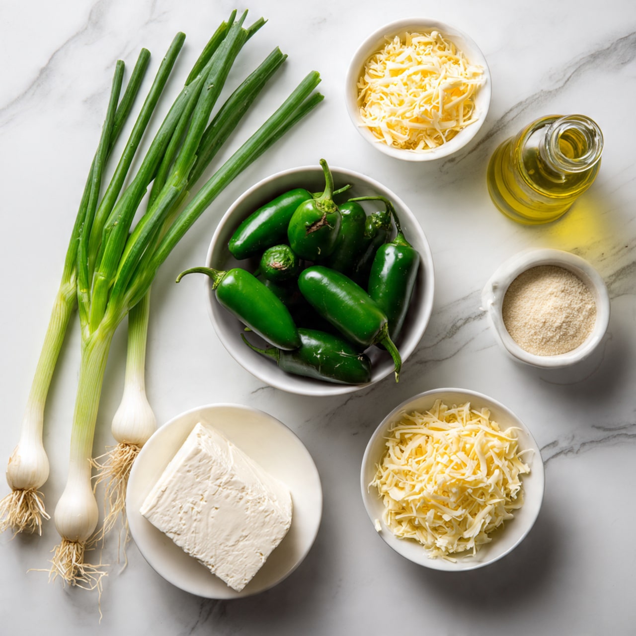 A white marbled surface holds an arrangement of fresh ingredients: a small white bowl filled with whole dark green jalapeno peppers at the center, two long green onions with white roots lying to the left side, a white bowl containing a solid block of cream cheese at the bottom right, and three small white bowls placed near the top right. One bowl has shredded yellow cheese, another has shredded white cheese, and the last bowl holds a light beige powder. A clear glass bottle with light yellow oil is also near the top right above the bowls. The photo taken with an iphone --ar 4:5 --v 7