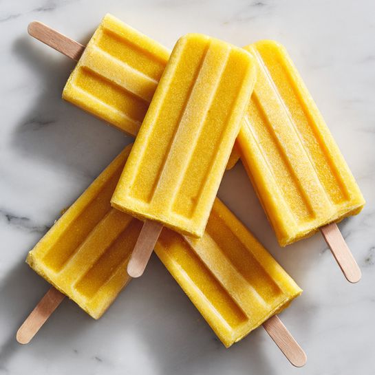 The image shows five bright yellow popsicles with a smooth, slightly shiny texture. Each popsicle has vertical grooves on one side and a wooden stick at the bottom, made from light-colored wood. One popsicle is placed on top, angled diagonally, fully visible with a flat front surface. The other four popsicles are partially visible beneath it, arranged on a white marbled surface. The photo is well-lit, showing the fresh and cool look of the popsicles. photo taken with an iphone --ar 4:5 --v 7