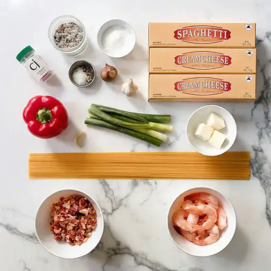 The image shows raw ingredients on a white marbled surface arranged neatly in rows. There are two small white bowls, one filled with cooked, chopped bacon pieces at the bottom left and the other with raw shrimp at the bottom right. Above them, there is a clove of garlic and a whole bulb of garlic next to a red bell pepper and two whole green onions. To the right, a small white bowl holds cubed pieces of butter. Above that are three rectangular boxes of cream cheese, one of which is open to show its edges. In the top left corner, a small jar of seasoning labeled