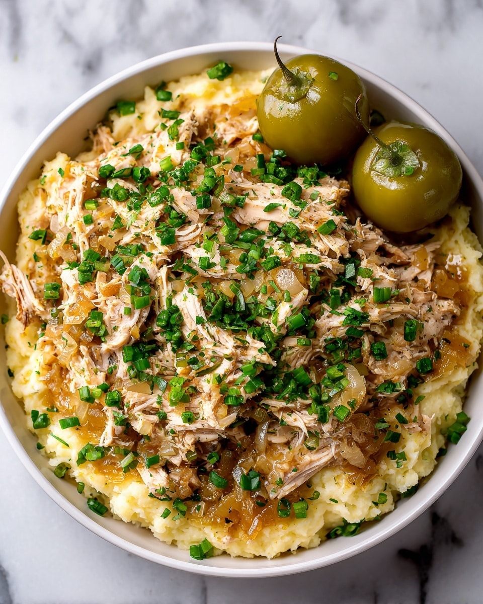 A white plate holds a base layer of smooth, creamy white mashed potatoes spread evenly in a shallow circle. On top of the mashed potatoes sits a generous layer of shredded light brown meat mixed with small chunks of cooked onions and a few green peppers scattered throughout. The meat layer is moist and slightly chunky with visible fibers and small bits of sauce pooling slightly around the edges. The dish is finished with a sprinkle of finely chopped fresh green herbs scattered on the top and around the plate. The plate sits on a white marbled surface with a small portion of leafy green herbs in the corner. Photo taken with an iphone --ar 4:5 --v 7