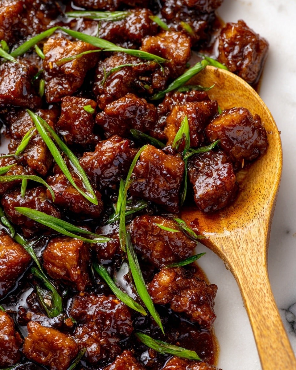 A close-up view of many small pieces of cooked meat coated in a thick, shiny dark brown sauce, scattered with thin slices of bright green scallions. The pieces have a glossy texture with some slight char marks, showing a rich caramelized look. A wooden spoon with a smooth surface is partially dipped into the meat and sauce from the right side. The whole scene is set against a white marbled background. photo taken with an iphone --ar 4:5 --v 7