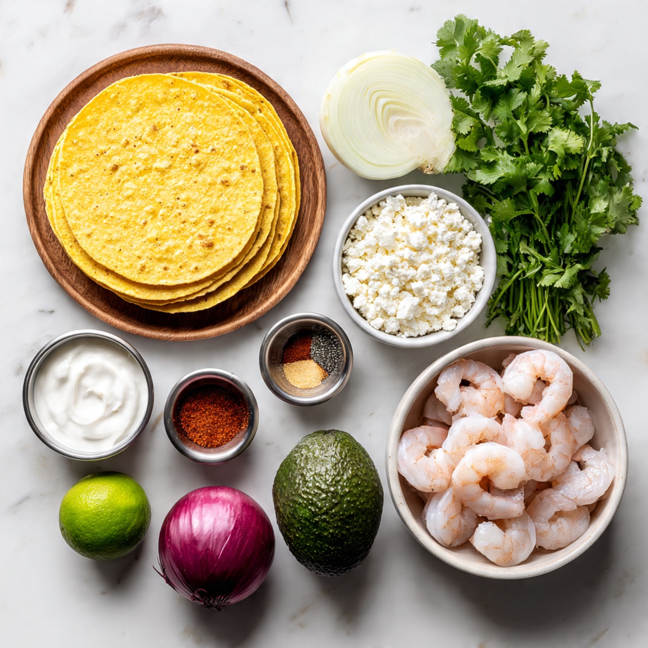 The image shows ingredients for a shrimp taco meal arranged neatly on a white marbled surface. On the left, there is a stack of yellow corn tortillas on a round wooden plate, next to fresh green cilantro bunches. Around the center, there is a small bowl of white crumbled cheese, a small metal cup of thick white sour cream, half a red onion, two whole green limes, and a metal cup of mixed spices including red, black, and beige powders. On the right side, a whole dark green avocado and two garlic cloves sit near a white bowl filled with peeled, uncooked shrimp that are pale pink and slightly translucent. There is also a slice of a white onion above the sour cream. The layout is clean and bright, with all ingredients visible clearly in their distinct colors and textures. photo taken with an iphone --ar 4:5 --v 7