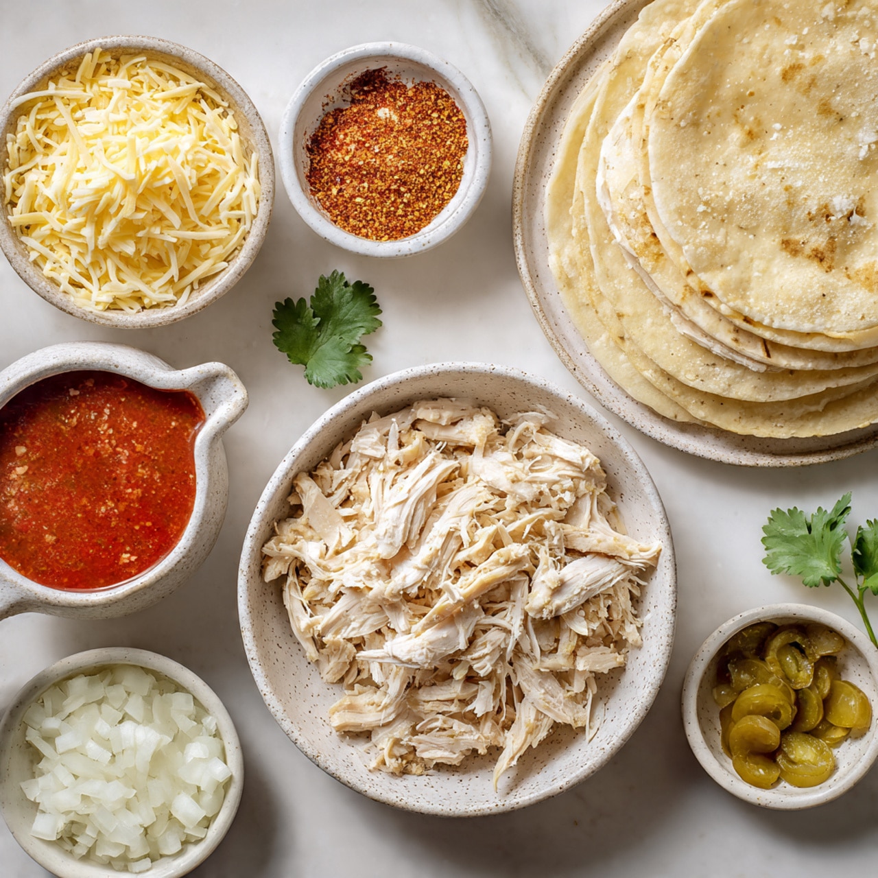 A white speckled bowl in the center holds shredded white chicken arranged loosely with soft, uneven strips. To its left is a smaller white speckled bowl full of mixed shredded cheese in yellow and white shades, with the texture thin and stringy. Below the cheese bowl is a white cup with a handle, filled with thick bright red sauce. Above the chicken bowl is a small white speckled bowl filled with a red and orange spice powder with a fine texture. To the right of the spice bowl is a large white speckled plate stacked with light beige, soft tortilla strips overlapping in layers. Below this tortilla plate is another small white speckled bowl filled with finely chopped white onions, each piece smooth and irregularly shaped. Small bowls with chunky light green pickled peppers and golden olive oil appear partially in the frame around the corners. Fresh green cilantro leaves rest beside the cheese bowl on a white marbled surface. photo taken with an iphone --ar 4:5 --v 7