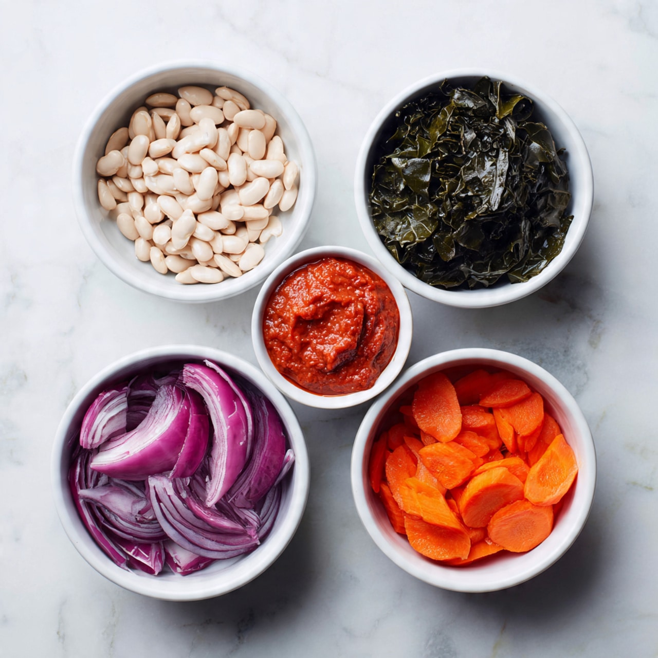 The image shows five white bowls arranged on a white marbled surface, each bowl holding a different ingredient. The top left bowl contains light-colored white beans, the top right smaller bowl holds red tomato paste with a smooth texture, the middle right bowl has dark green leafy greens with a slightly wrinkled texture, the bottom left bowl is filled with sliced red onions that have purple and white layers, and the bottom right bowl contains bright orange carrot slices. The bowls are neatly placed to show the colors and textures of each ingredient clearly photo taken with an iphone --ar 4:5 --v 7