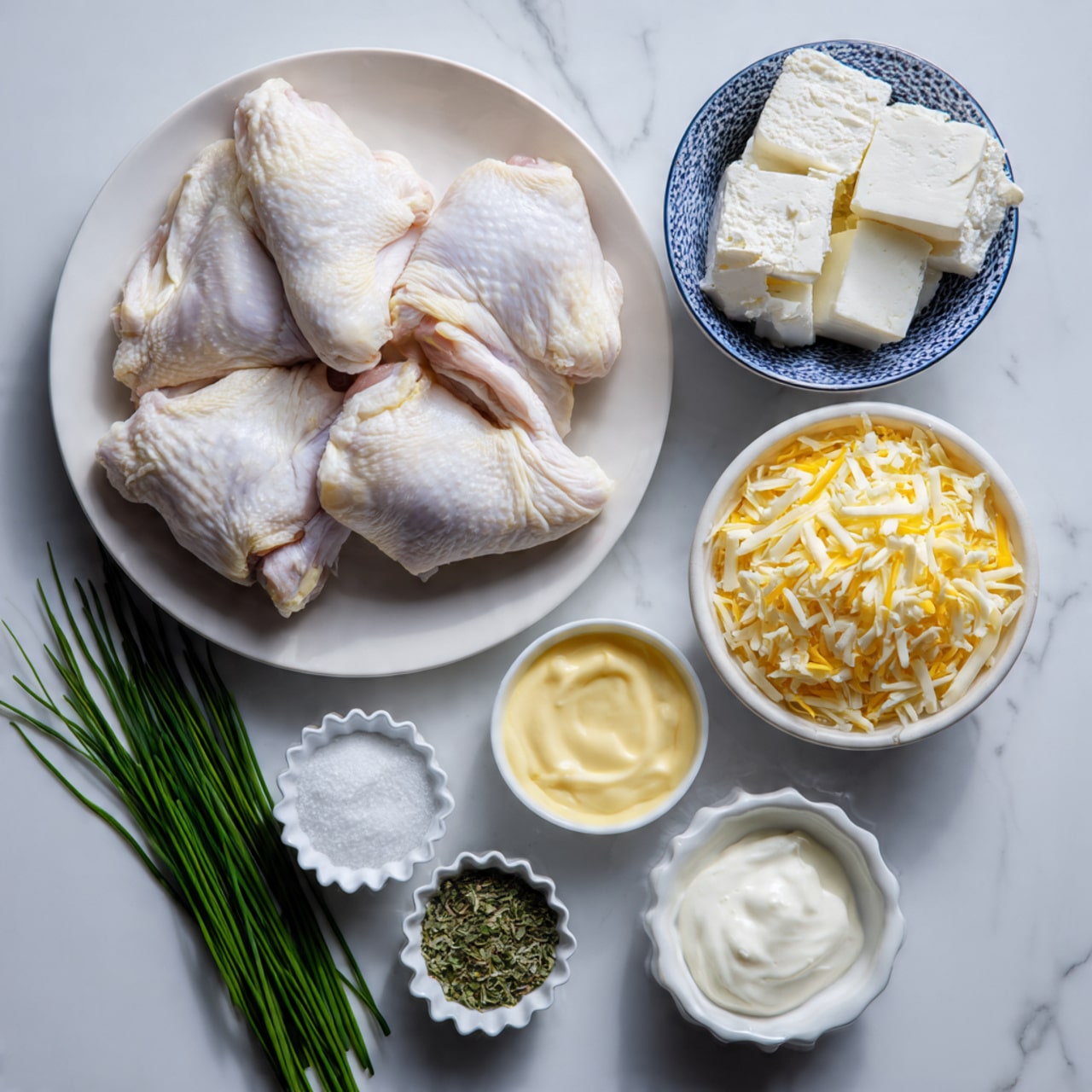 A white plate on a white marbled surface holds four raw chicken fillets laid side by side. Next to it, a small white bowl with dark blue patterns contains three big blocks of cream cheese. To the right, a white bowl is full of shredded orange and white cheese. Below these bowls, there are four smaller white dishes holding fresh green chives, a mix of dried spices, salt, thick white sour cream, and smooth yellow mayonnaise. The colors and textures create a clean and fresh look. Photo taken with an iphone --ar 4:5 --v 7