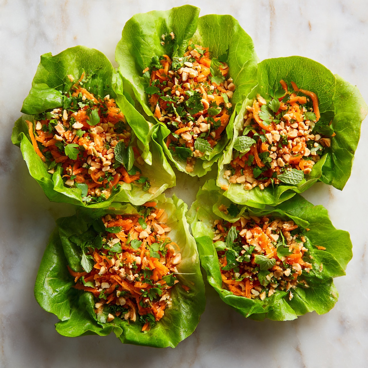 Five bright green lettuce leaves are arranged in a circle on a white marbled surface, each leaf filled with a mix of shredded orange carrots, finely chopped nuts, and small green herbs. The carrot mixture looks fresh and textured, topped with scattered crushed nuts that add a crunchy appearance. The lettuce leaves have a fresh, crisp look, wrapping the mixture gently, and small green herbs are dotted on the surface. The overall look is colorful, fresh, and inviting. photo taken with an iphone --ar 4:5 --v 7
