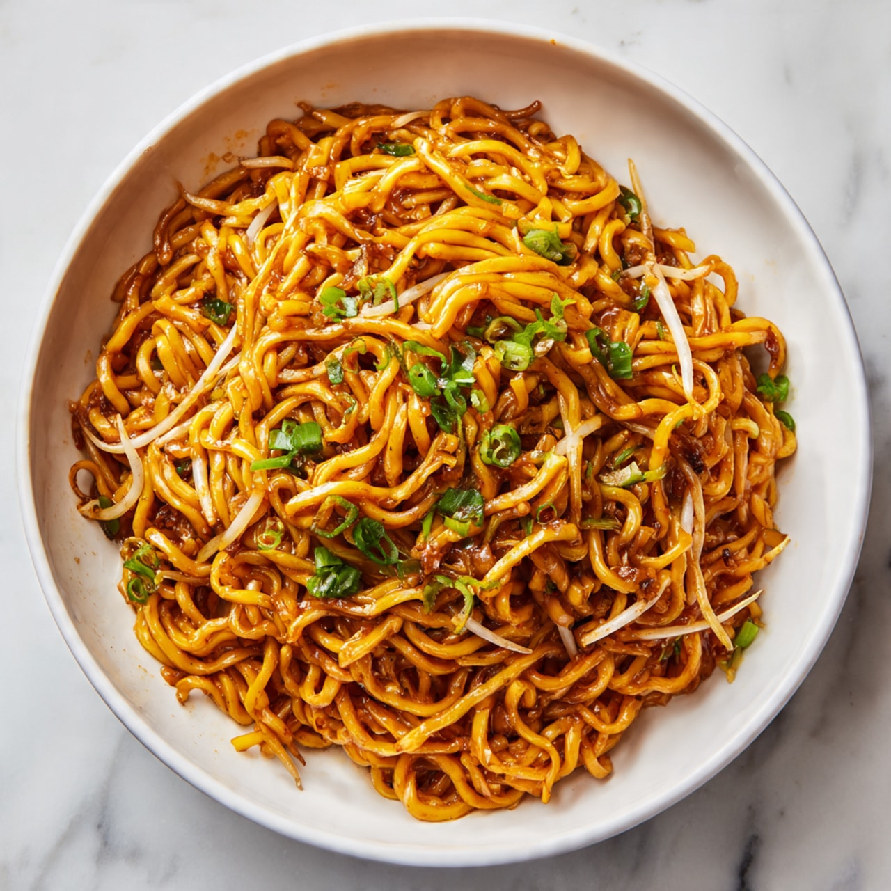 A white bowl is filled with thick, twisted yellow noodles coated in a shiny sauce that gives them a rich orange-brown color. Mixed within the noodles are thin white bean sprouts and small pieces of green onion, adding contrast and texture. The noodles are piled high, twisted into a loose mound in the center of the bowl, with the vegetables scattered evenly throughout. The bowl rests on a white marbled surface. photo taken with an iphone --ar 4:5 --v 7