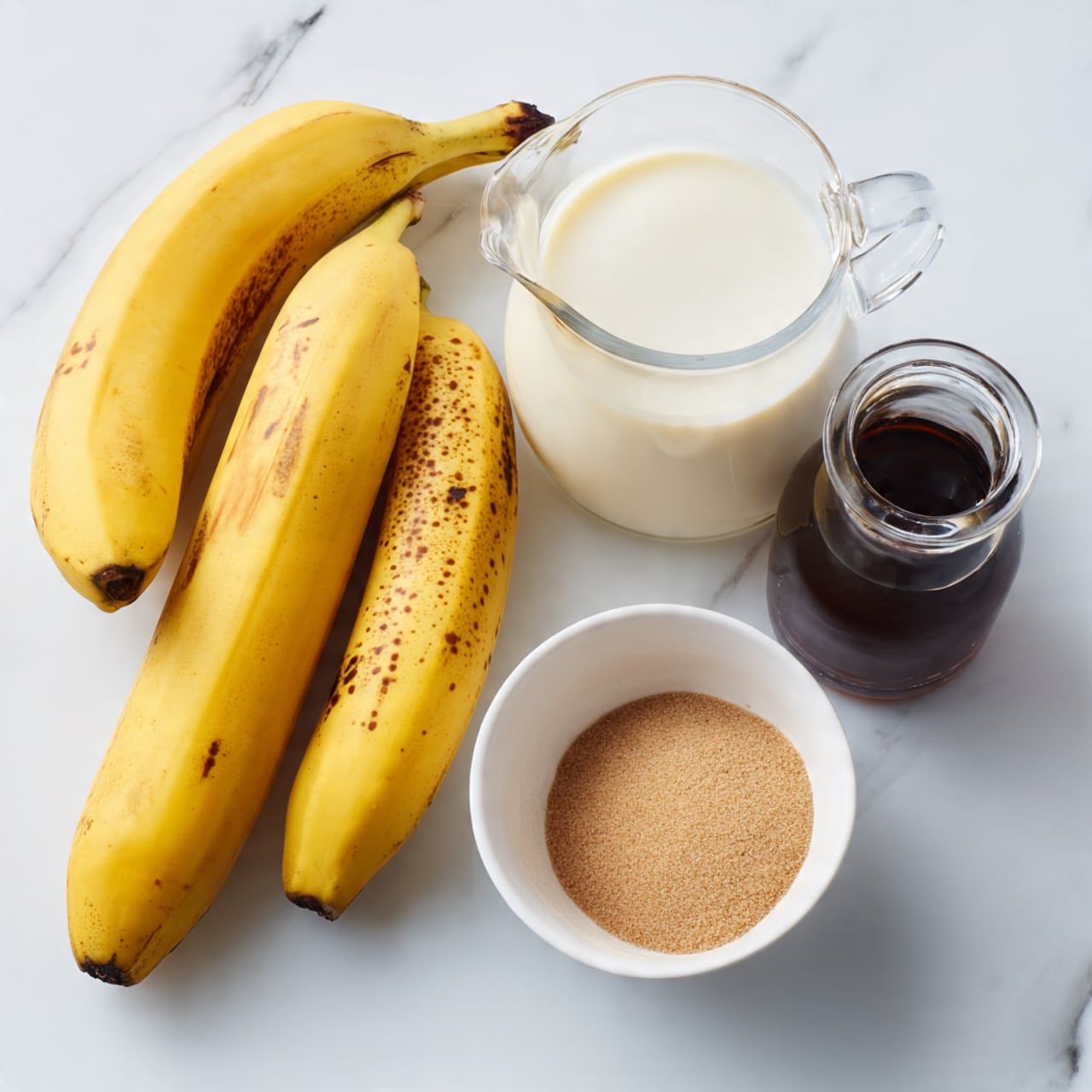 The image shows four yellow bananas with some brown spots, placed together on a white marbled surface. Next to the bananas is a clear glass jug with white milk, a white small bowl filled with light brown sugar, a clear empty glass jug, and a dark brown bottle of vanilla extract. The items are arranged spaced apart clearly on the white marbled surface, providing a clean and simple look. photo taken with an iphone --ar 4:5 --v 7