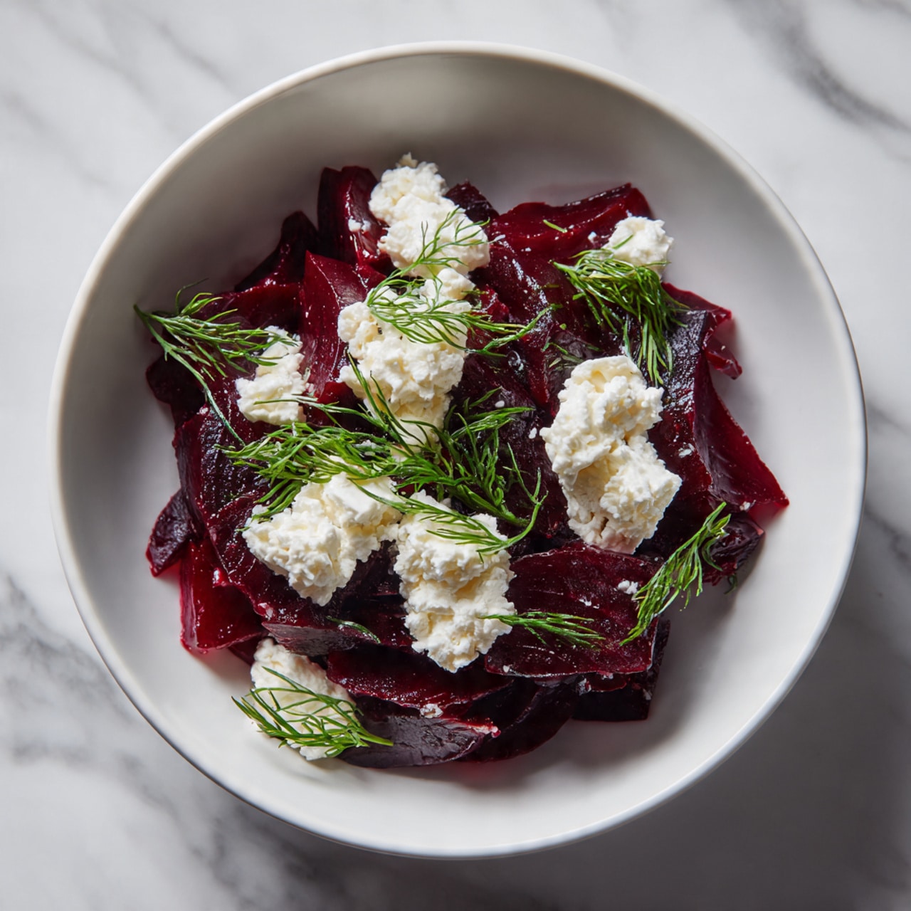 In a white bowl, there is a dish with two main layers. The bottom layer is made of dark red beet strips which look soft and slightly shiny. On top, there are small white dollops of cheese that look soft and crumbly. Fresh green dill sprigs are scattered around, adding a touch of color and fresh texture. The bowl sits on a white marbled surface. Photo taken with an iphone --ar 4:5 --v 7