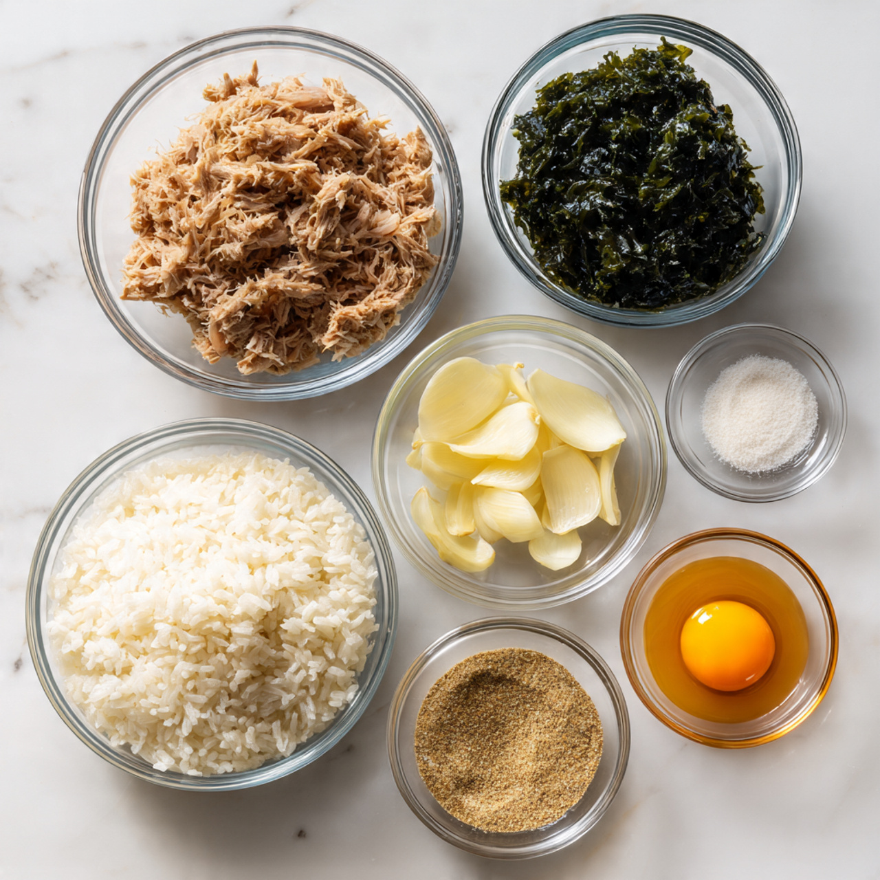The image shows seven clear glass bowls arranged neatly on a white marbled surface. In the largest bowl at the bottom left, there is a layer of white rice with a soft, fluffy texture. To the right of it and slightly above, a smaller bowl holds shredded tuna, brownish in color with some moisture. Above the tuna, a bowl contains chopped dark green seaweed with a slightly glossy texture. To the right of the seaweed, a small bowl has several pale yellow, smooth slices of garlic. Next to the garlic, a tiny bowl holds a white powder, likely salt, with a fine, grainy texture. Below the salt, a clear bowl contains a light brown, grainy spice or seasoning. Finally, at the far right, a small glass bowl has a raw egg yolk, bright orange-yellow and shiny. All bowls are placed on the white marbled surface in a balanced layout. Photo taken with an iphone --ar 4:5 --v 7