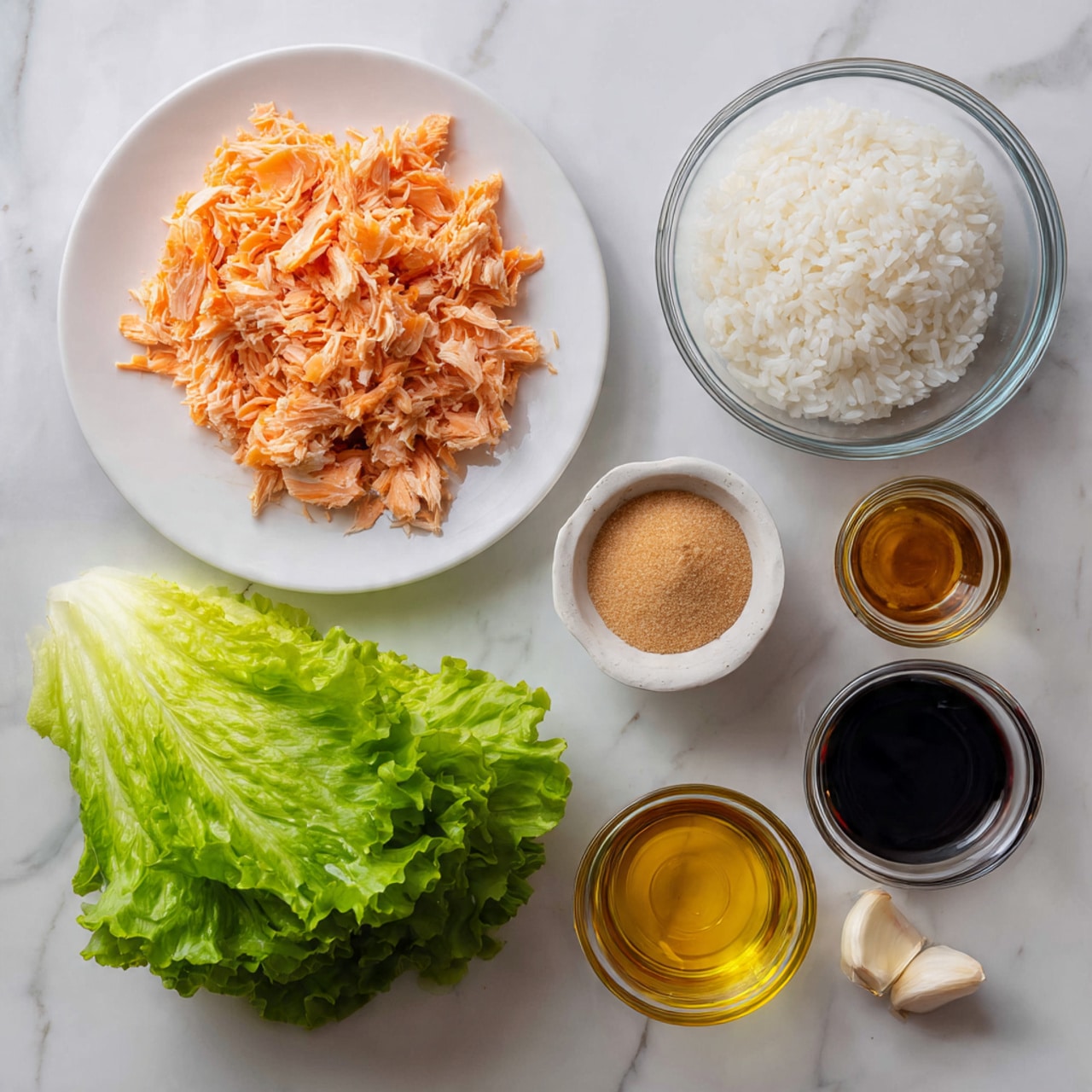 A collection of cooking ingredients is arranged on a white marbled surface, including a large white plate filled with shredded cooked salmon in warm light orange tones at the top left, a small white bowl with light brown sugar next to it, and a clear glass bowl with white cooked rice at the bottom right. Below the salmon plate is a bunch of fresh bright green lettuce leaves with soft texture. To the right of the sugar bowl are small metal and glass containers holding dark soy sauce, golden oil, and seasoning in amber and gold colors, plus a single peeled garlic clove on the surface. Everything is neatly placed and ready for food preparation photo taken with an iphone --ar 4:5 --v 7