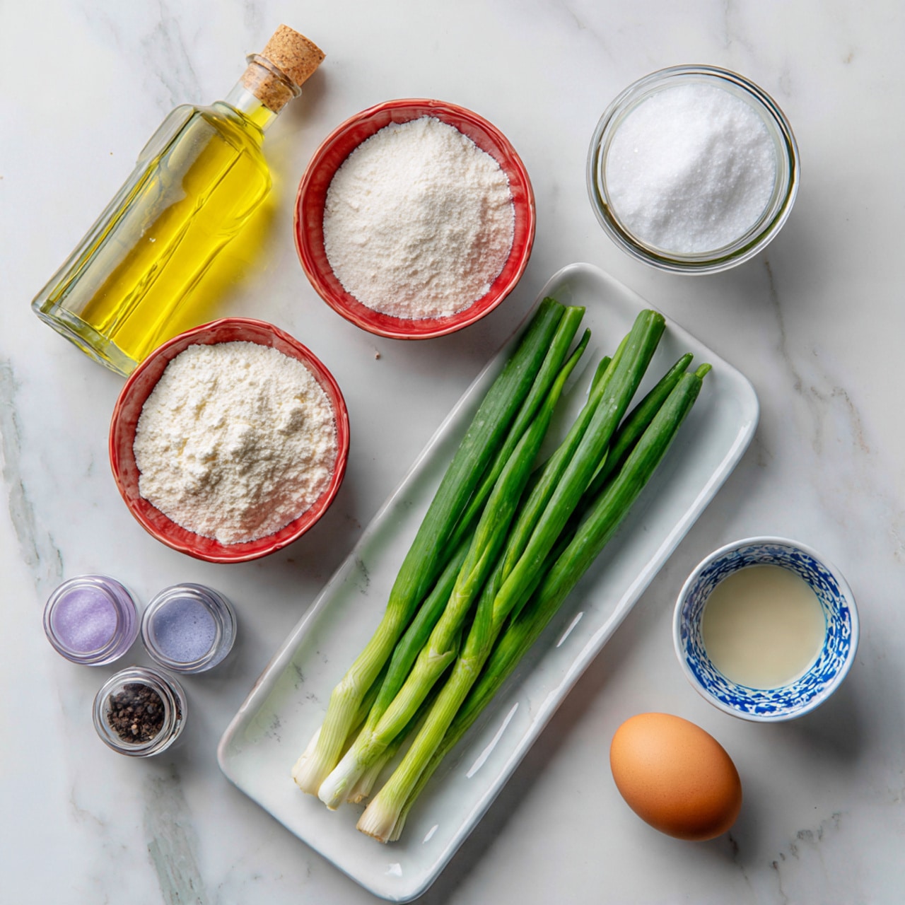 The image shows a white rectangular plate on a white marbled surface, holding six fresh green onions lined up in two rows and one brown egg placed at the bottom left of the plate. Above the plate are two red bowls filled with white powders, one with a coarser texture and the other finer, arranged side by side. Next to them is a glass jar filled with white granulated salt and another small white cup with a blue pattern containing a light beige liquid. On the left side, a bottle of clear yellow oil stands upright, and in front of it, two small clear spice jars with purple lids are visible. photo taken with an iphone --ar 4:5 --v 7