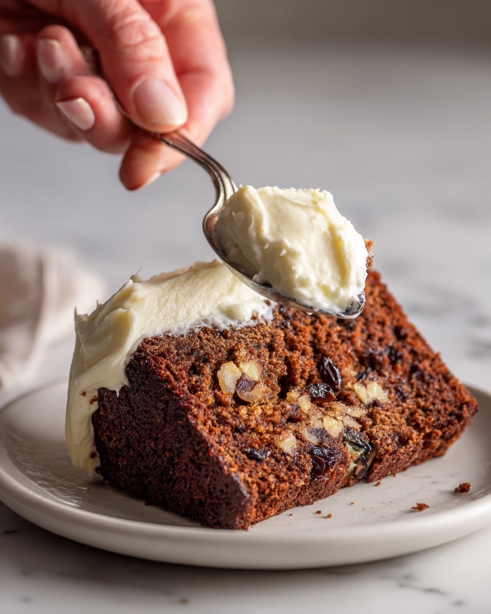 A close-up photo shows a thick slice of dark brown cake with visible bits of nuts and raisins inside. The cake slice sits on a white plate with a white marbled surface under it. On top of the cake, there is a creamy white spread that looks smooth and thick. A silver spoon, held by a woman's hand, has some of the cake and cream mixture on it, positioned above the plate. The lighting highlights the moist and textured inside of the cake. Photo taken with an iphone --ar 4:5 --v 7
