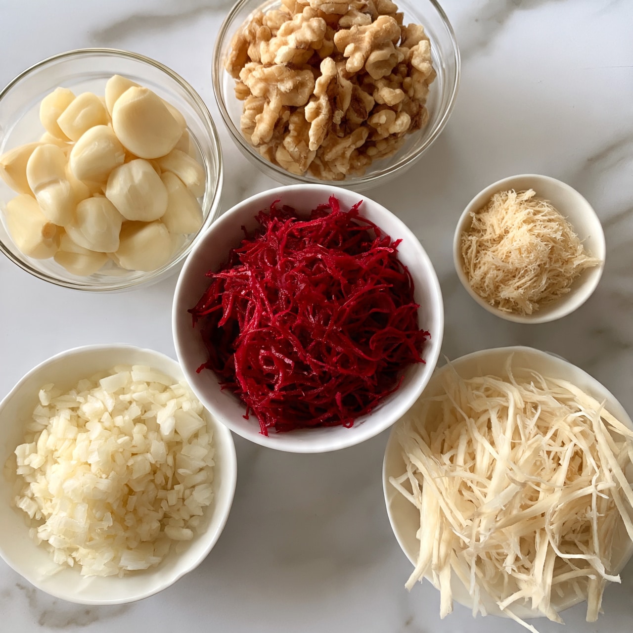 square image The image shows six small bowls arranged on a white marbled surface. In the center is a white bowl filled with bright red shredded beetroot, thin and stringy in texture. Above it, from left to right, are two glass bowls; one with whole peeled garlic cloves in a pale cream color, and another filled with light brown walnut pieces, uneven and textured. To the far right above the central bowl, a small white bowl contains a light beige shredded ingredient that looks fibrous. Below the central bowl, there are two more white bowls; one holds finely chopped white onions, and the other contains thin, pale off-white shredded strips that resemble root vegetables. The bowls and ingredients create a clean, organized look. Photo taken with an iphone --ar 4:5 --v 7square image