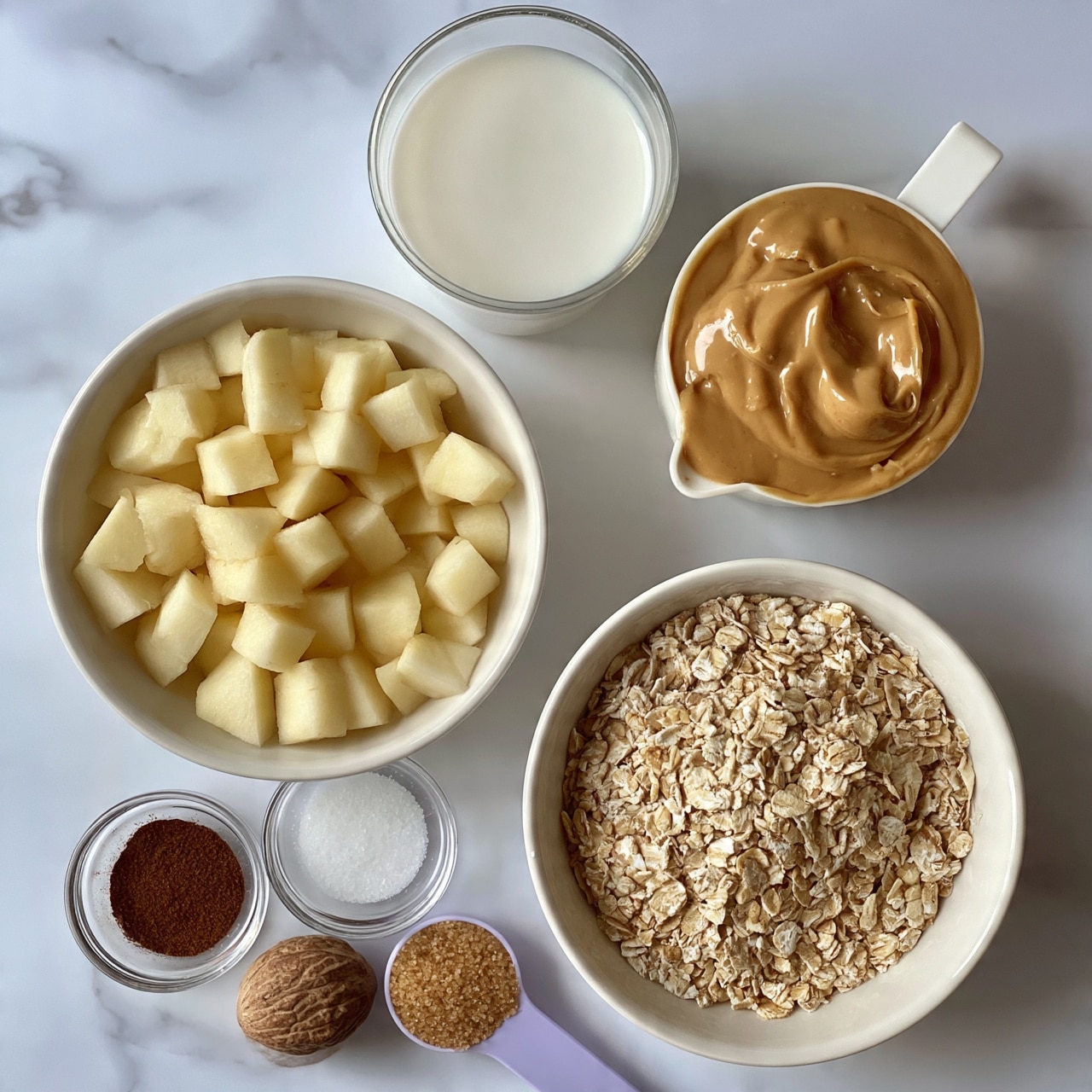 square image The image shows a top view of various ingredients placed on a white marbled surface. There are two medium-size white bowls, one filled with small light yellow apple cubes on the left and one filled with rolled oats at the bottom right. To the upper right, a white measuring cup holds smooth, light brown peanut butter. Above it, a clear glass cup is filled with white milk. Near the bottom left are two small clear glass bowls, one with dark brown spice powder and the other with white salt. Just below these bowls, a whole brown nutmeg is placed next to a lilac measuring spoon filled with light brown brown sugar. The colors are mostly light and neutral, with the textures ranging from soft and creamy to rough oats. The lighting is bright and even, giving a clean and fresh look. Photo taken with an iphone --ar 4:5 --v 7