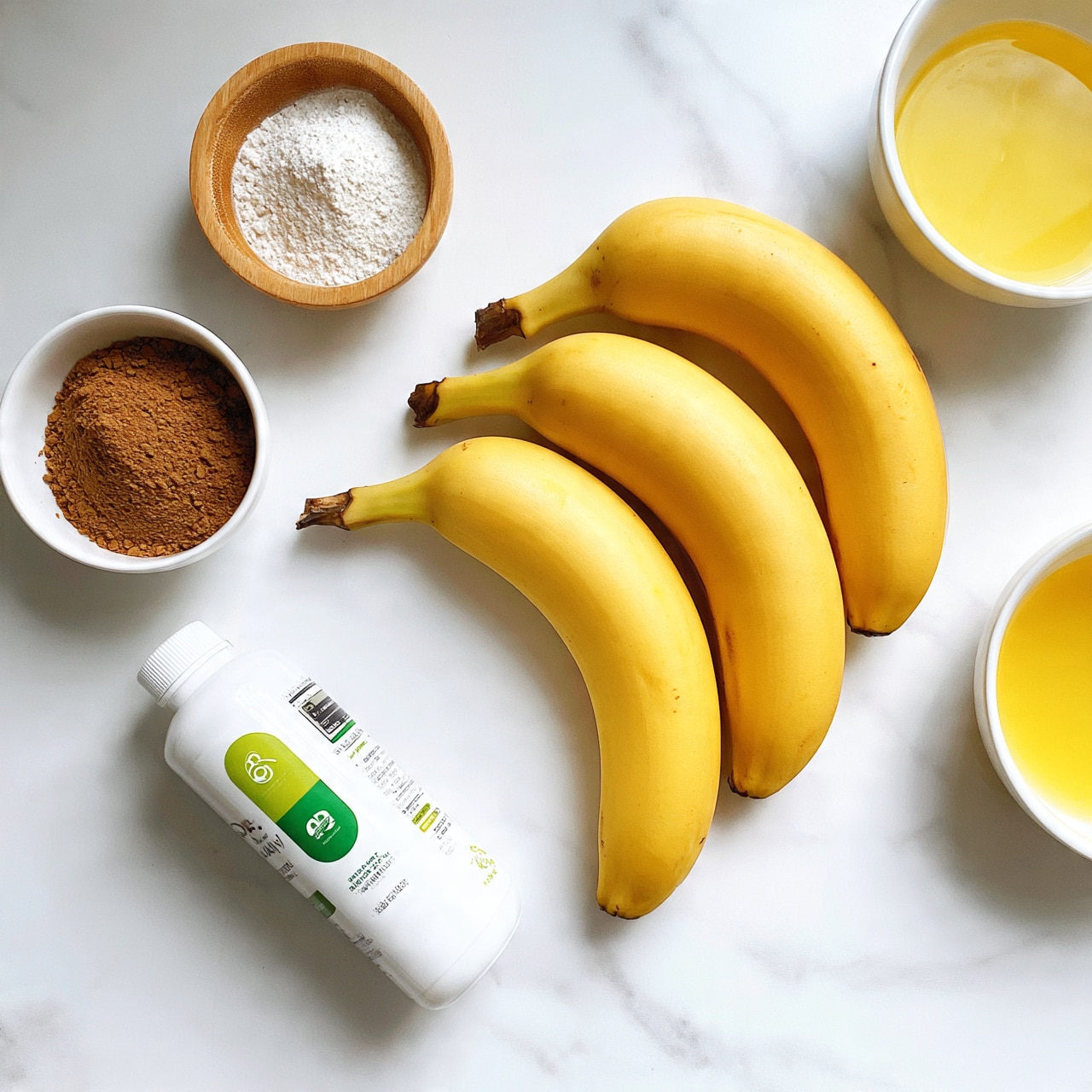square image The image shows three bright yellow bananas with smooth skins placed on a white marbled surface. Near the bananas, there is a white bottle with green and black text and images on it, lying horizontally. To the left, a small white bowl holds a mound of brown powder, and above it is a small round wooden bowl filled with a white fine powder. To the right, a small white bowl contains a yellow liquid. The whole scene is brightly lit and clean, with all items resting on a white marbled background. Photo taken with an iphone --ar 4:5 --v 7